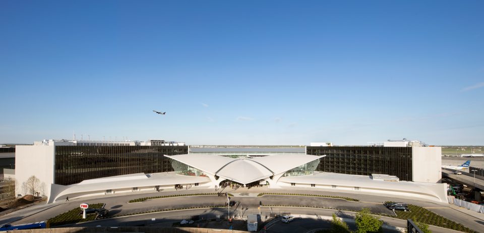 Photo of TWA Flight Center exterior with two glass and concrete rectangular hotel structures behind it