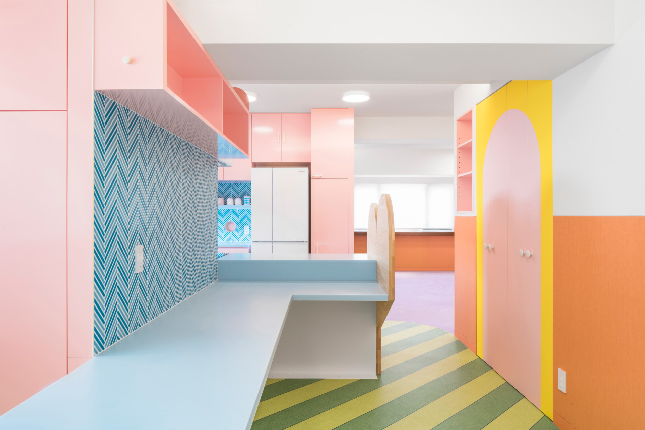 A pastel pink kitchen with blue tile backsplash and green striped floors