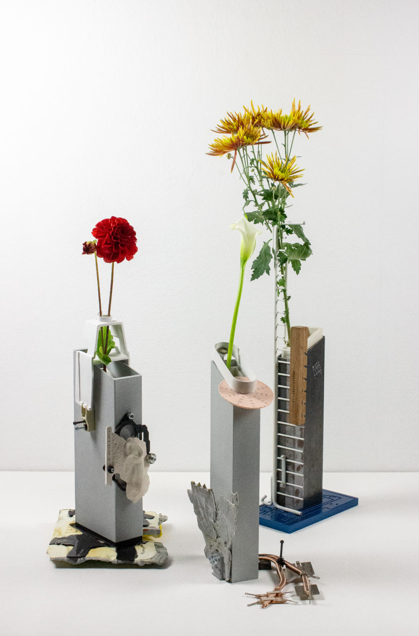 A series of angular vases holding different type of flowers in front of a white backdrop