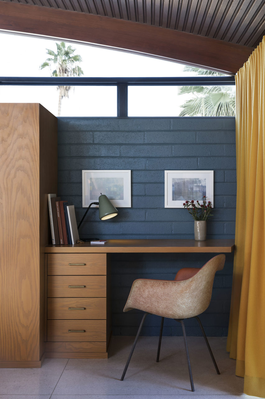 image of a chair and desk in front of blue brick wall with ceiling level windows and a yellow curtain