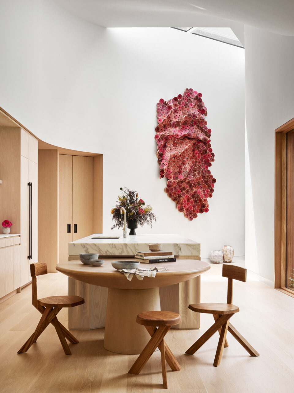 A bright wall sculpture overlooks a wooden dining table and kitchen