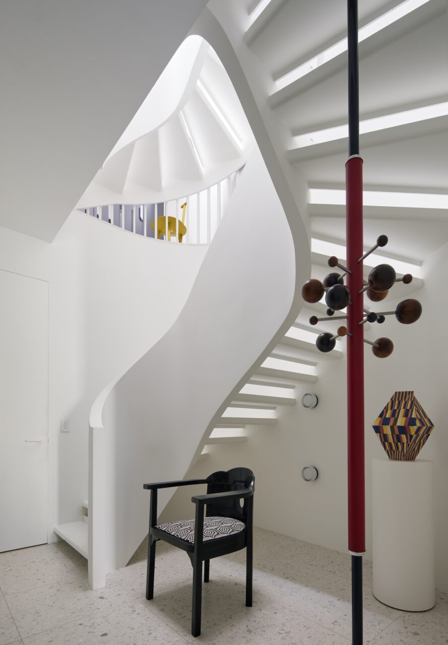 A curving staircase ends with a chair and standing lamp