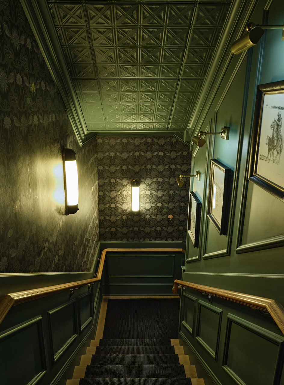 A green stairwell with silk-screened wallpaper leads to Auric Room 1915