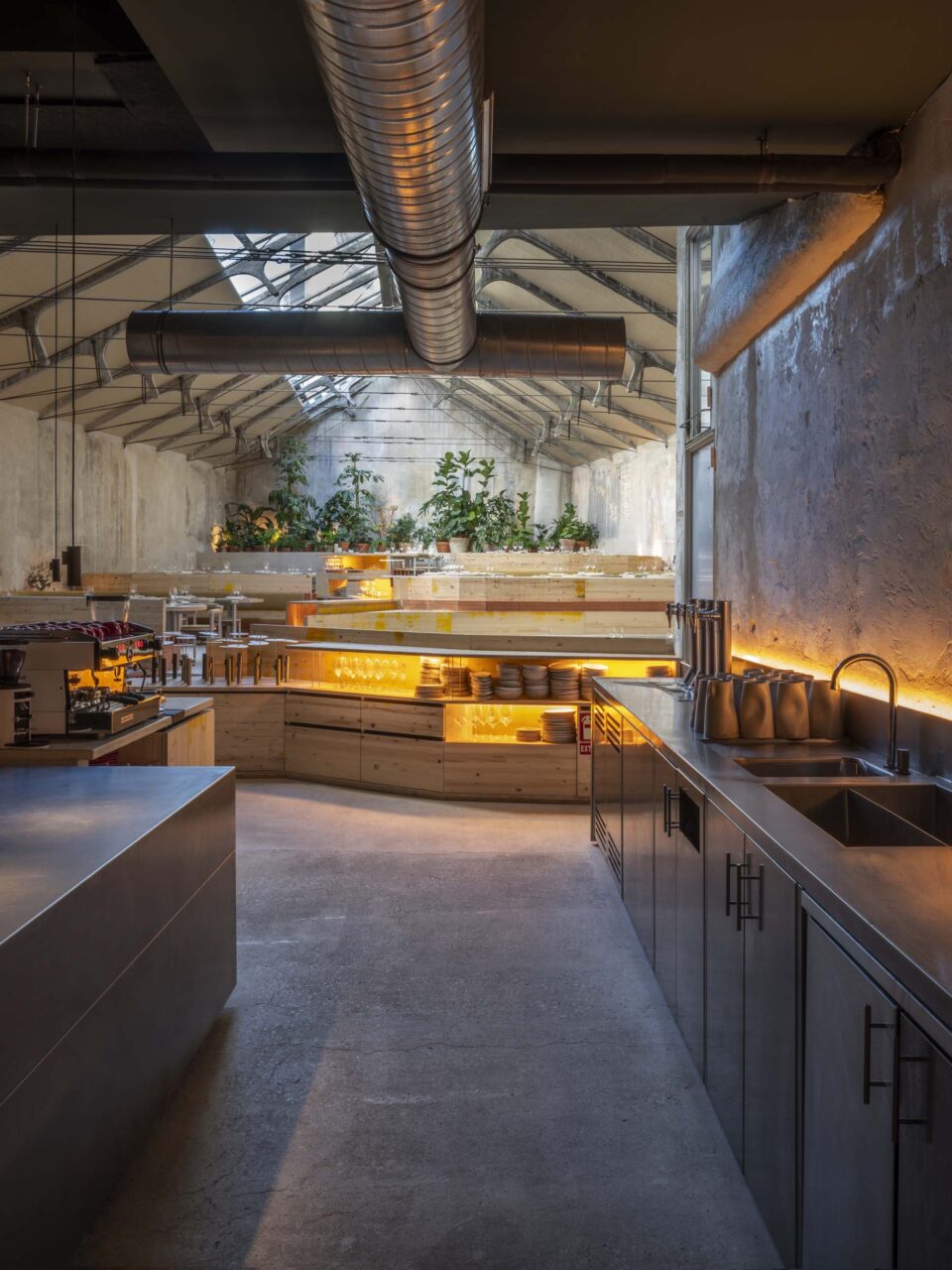 A dim core of a restaurant gives way to the skylight-lit end under tall, gabled ceilings
