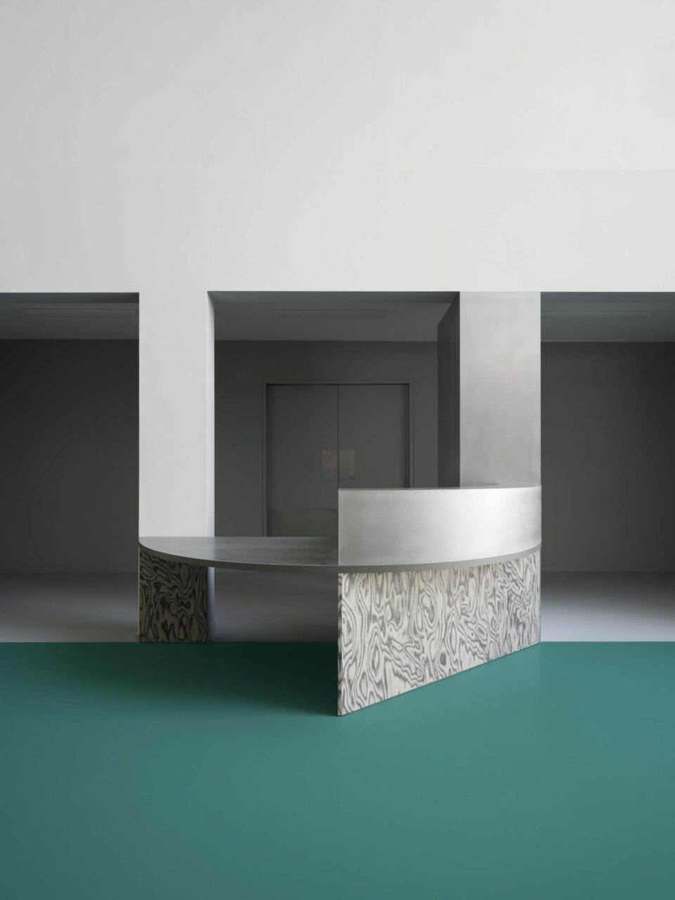 On teal floors, a curving table with steel greets the entrance of FOMU