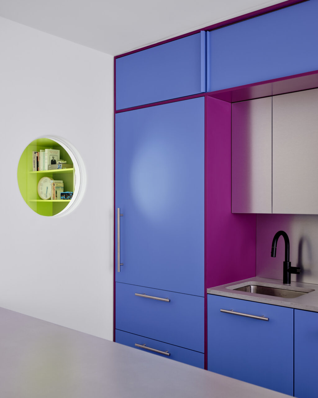 A porthole in a blue kitchen reveals a green flex room