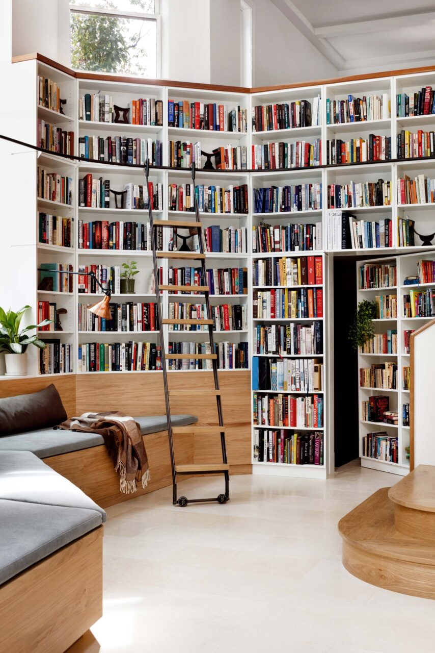 A wall of books with a ladder and banquette at Cleveland Park House