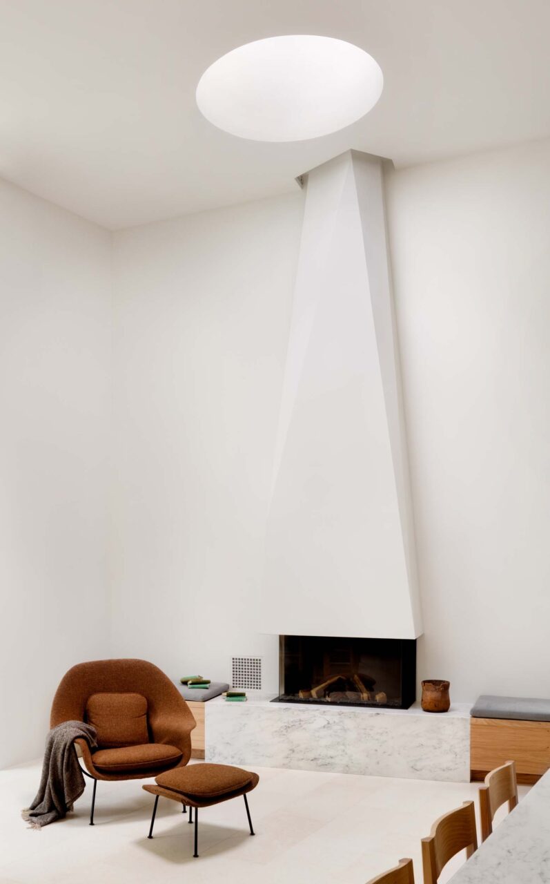 A white room with a sculptural fireplace and lounge chair at Cleveland Park House