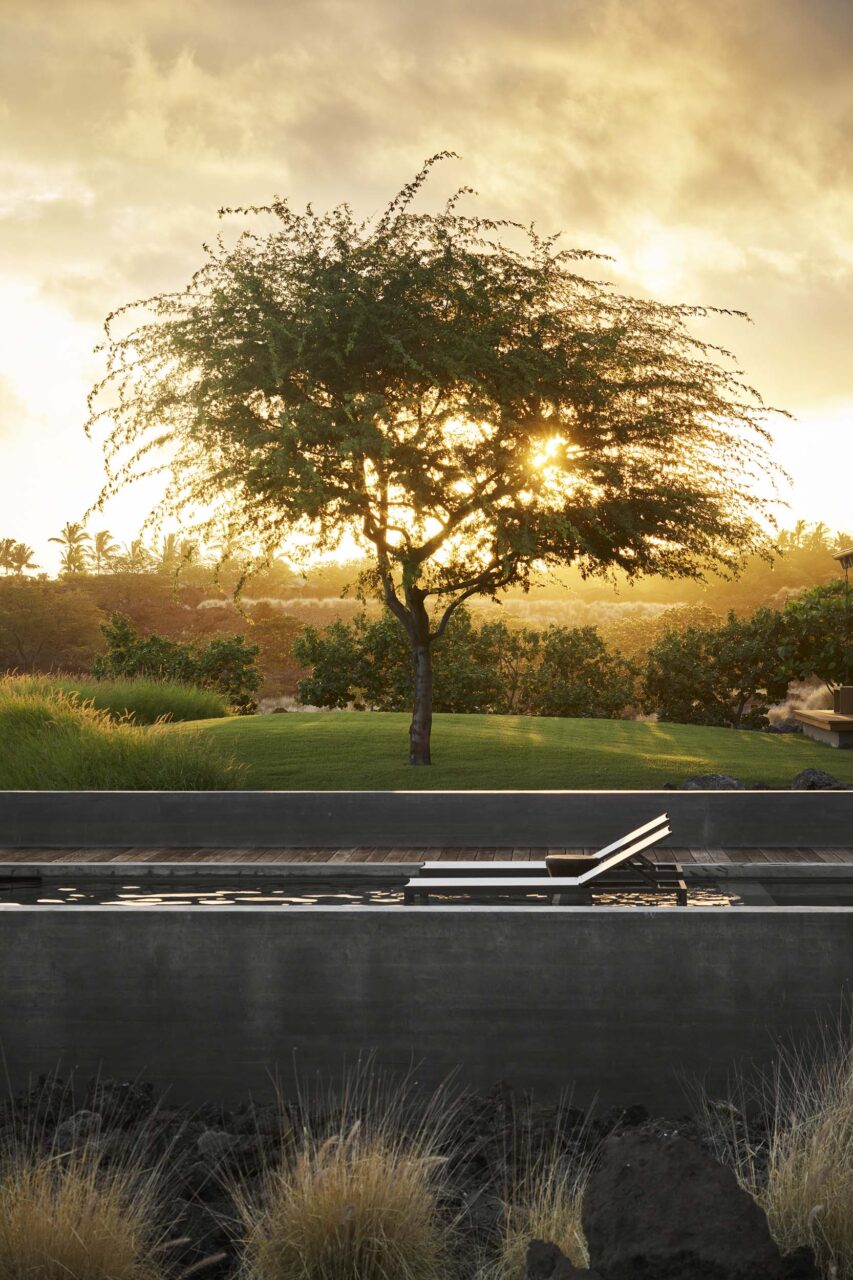 Under a sunset, lounge chairs sit by a long, slender pool at Hale Kiawe