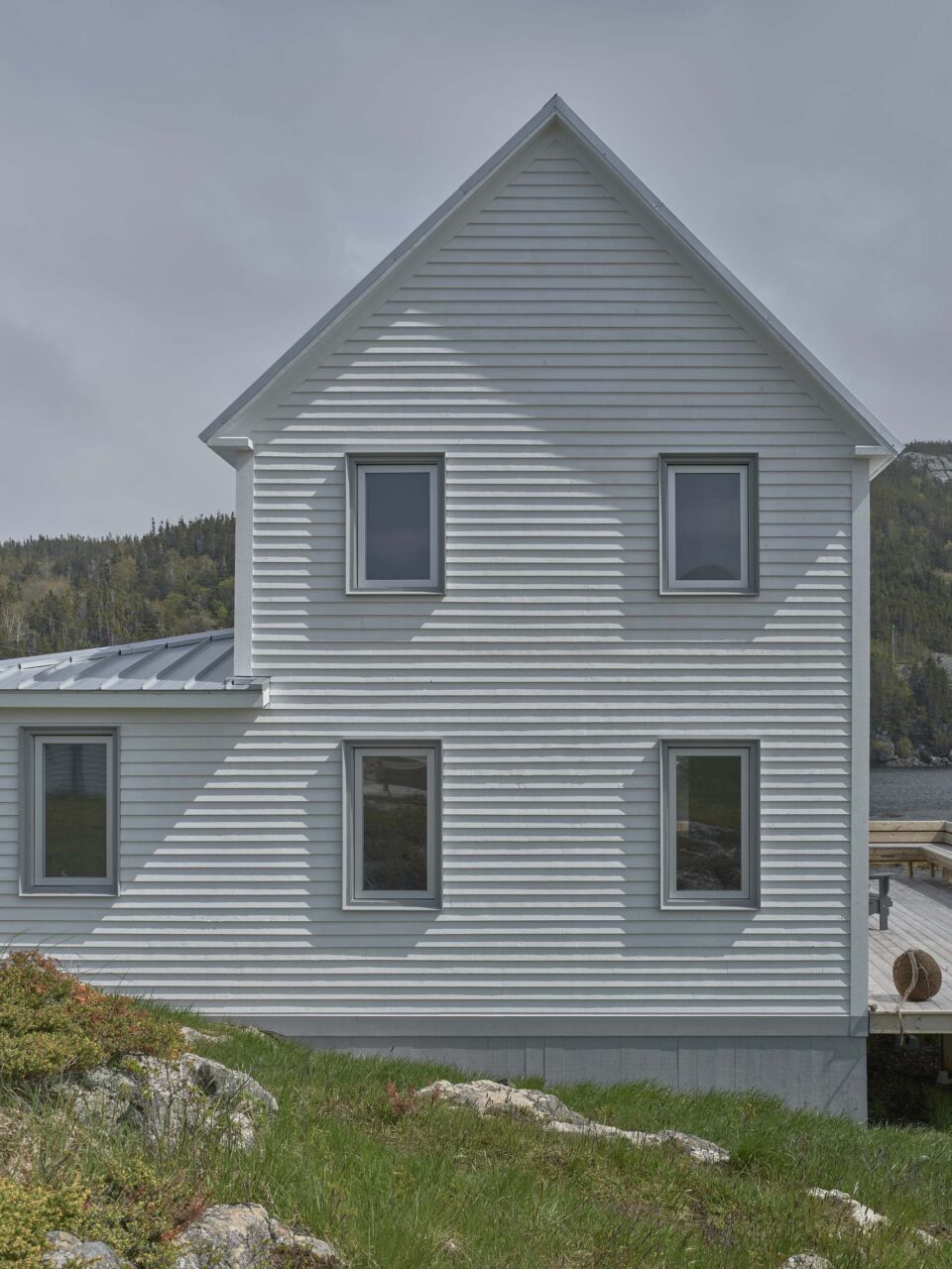 Small, numerous windows grace the side of a saltbox home by Reflect Architecture