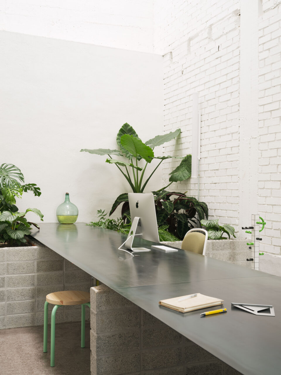 At RABE, a macbook sits on a long table and surrounded by plants