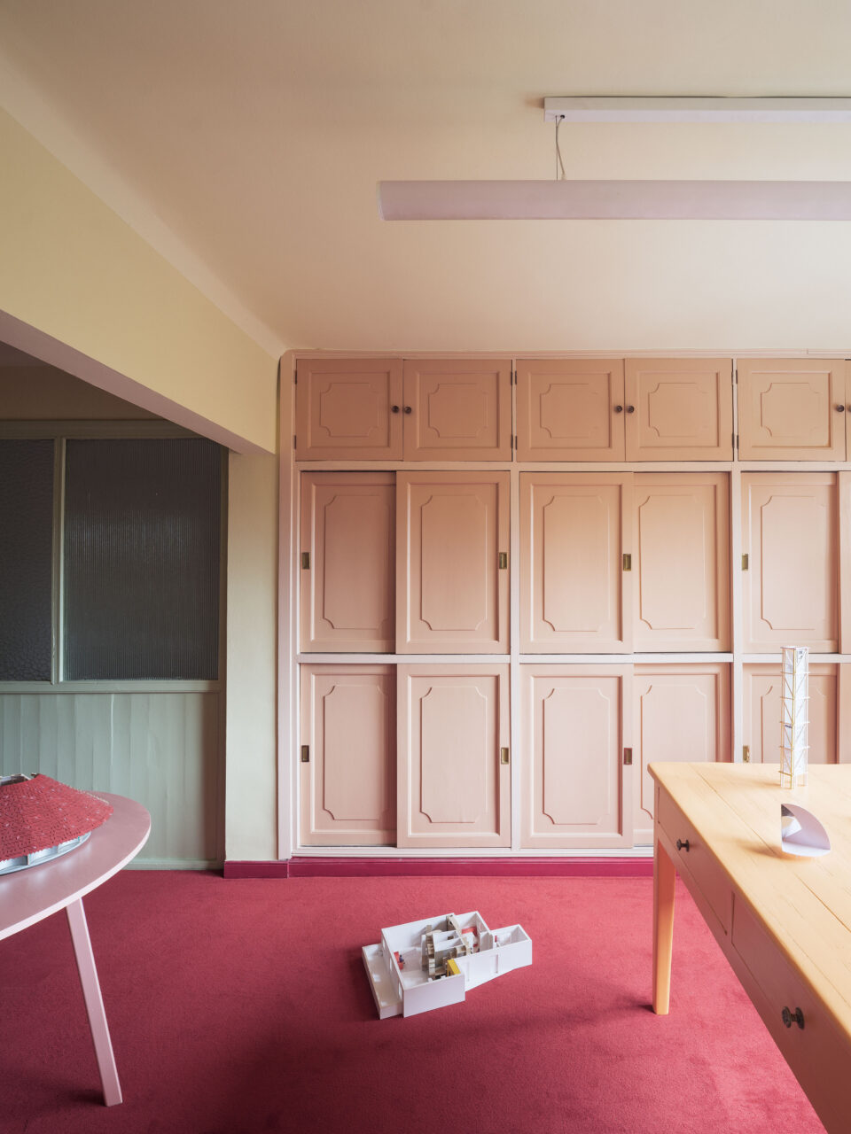 A pink wall of cabinets sits in a room with a darker pink rug in RABE