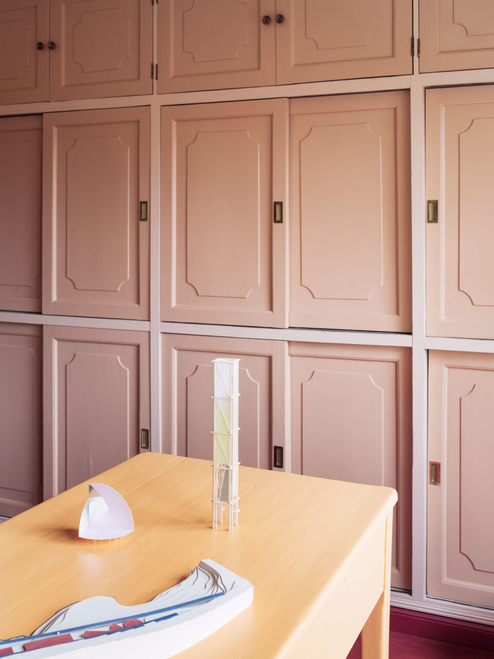 In front of pink cabinets, a table holds models from BeAr Architects