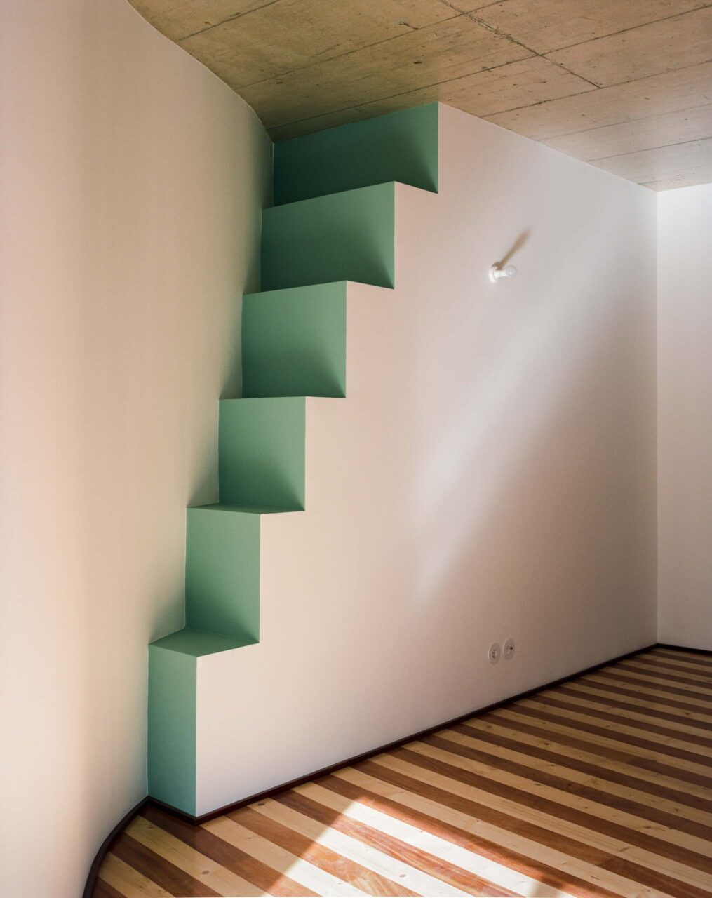 A side of a room with steps that lead to nowhere along the wall by Fala Atelier