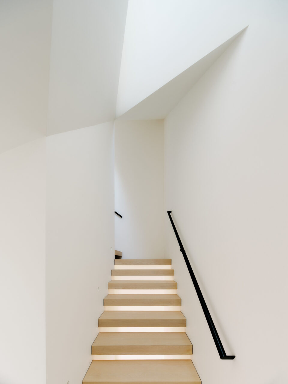 A white and wooden stairwell with cut-out planes in the ceiling