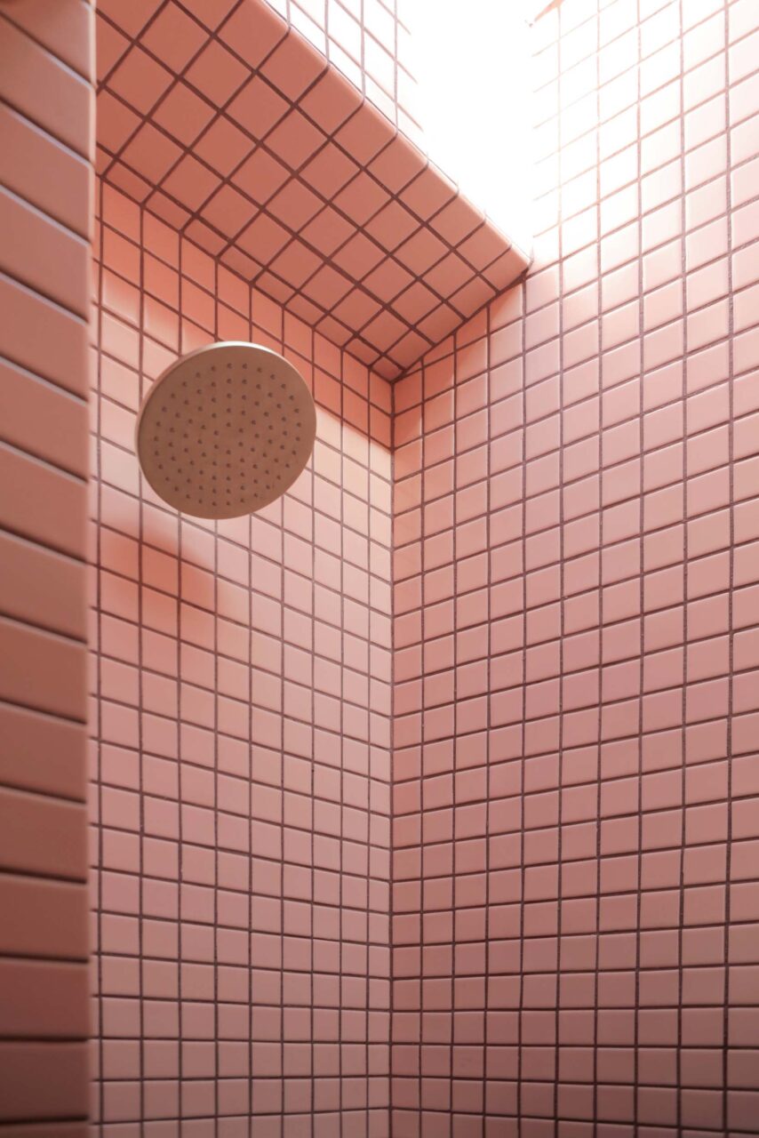 A pink tiled shower with light coming down