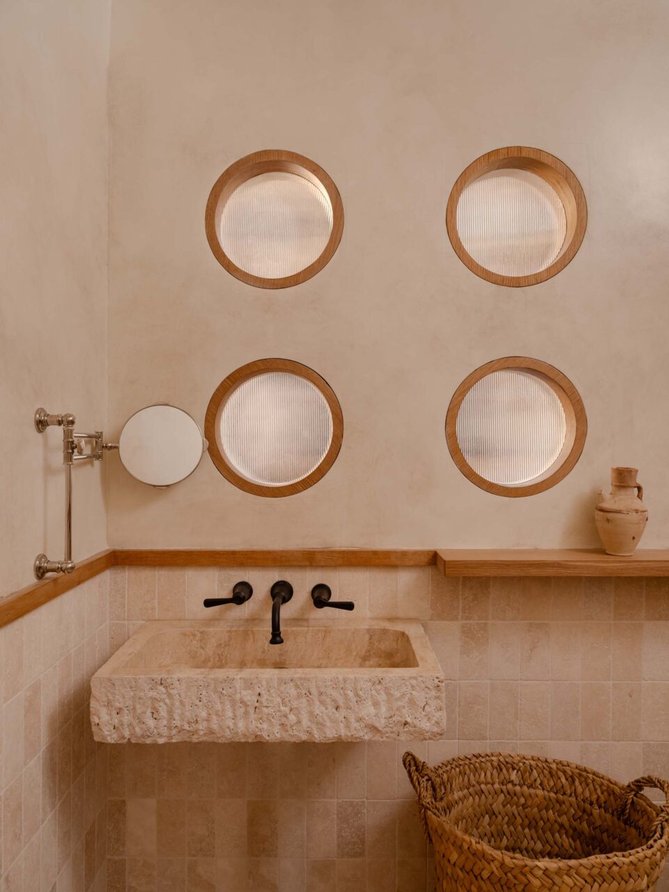 A bathroom at Theodora features portholes, tiles, and earthy, neutral tones.
