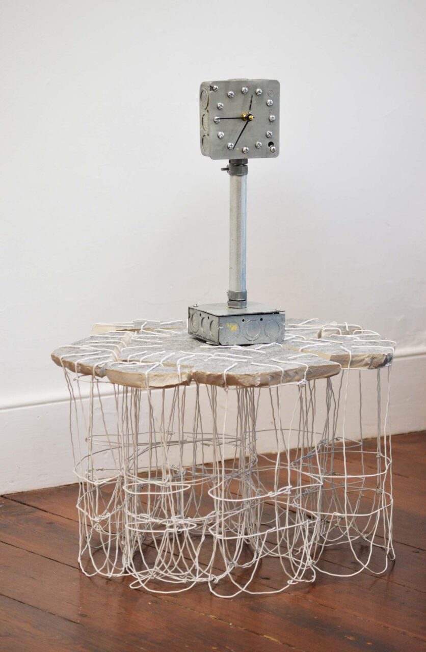 A wire mesh table with a clock made from a junction box by William Stone